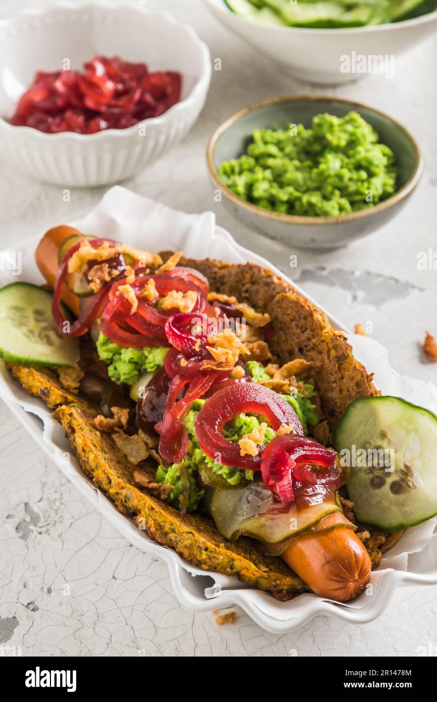 Chien chaud végétarien sain avec pain plat à base de légumes, recouvert d'oignons rouges, de cornichons et de purée de pois, fond blanc Banque D'Images