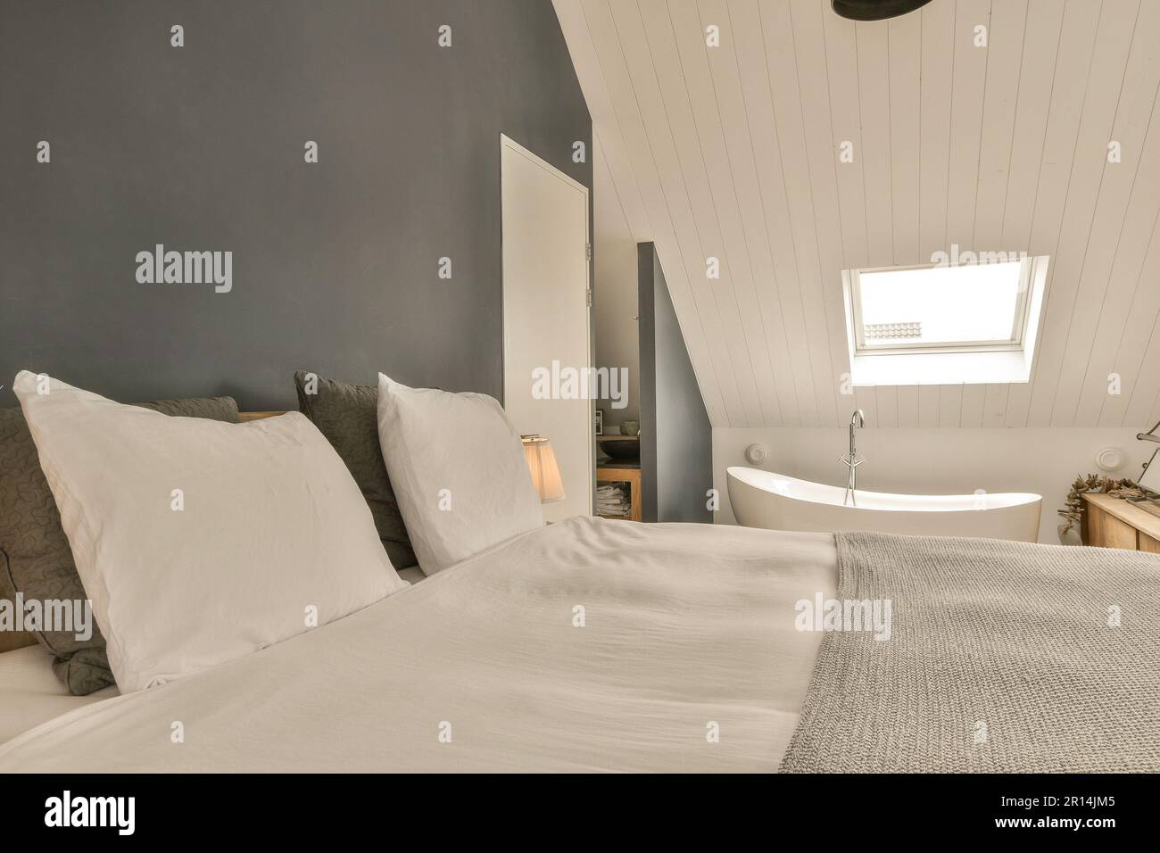 lit avec draps et oreillers blancs dans une chambre aux murs bleus, parquet et baignoire sur le côté droit Banque D'Images