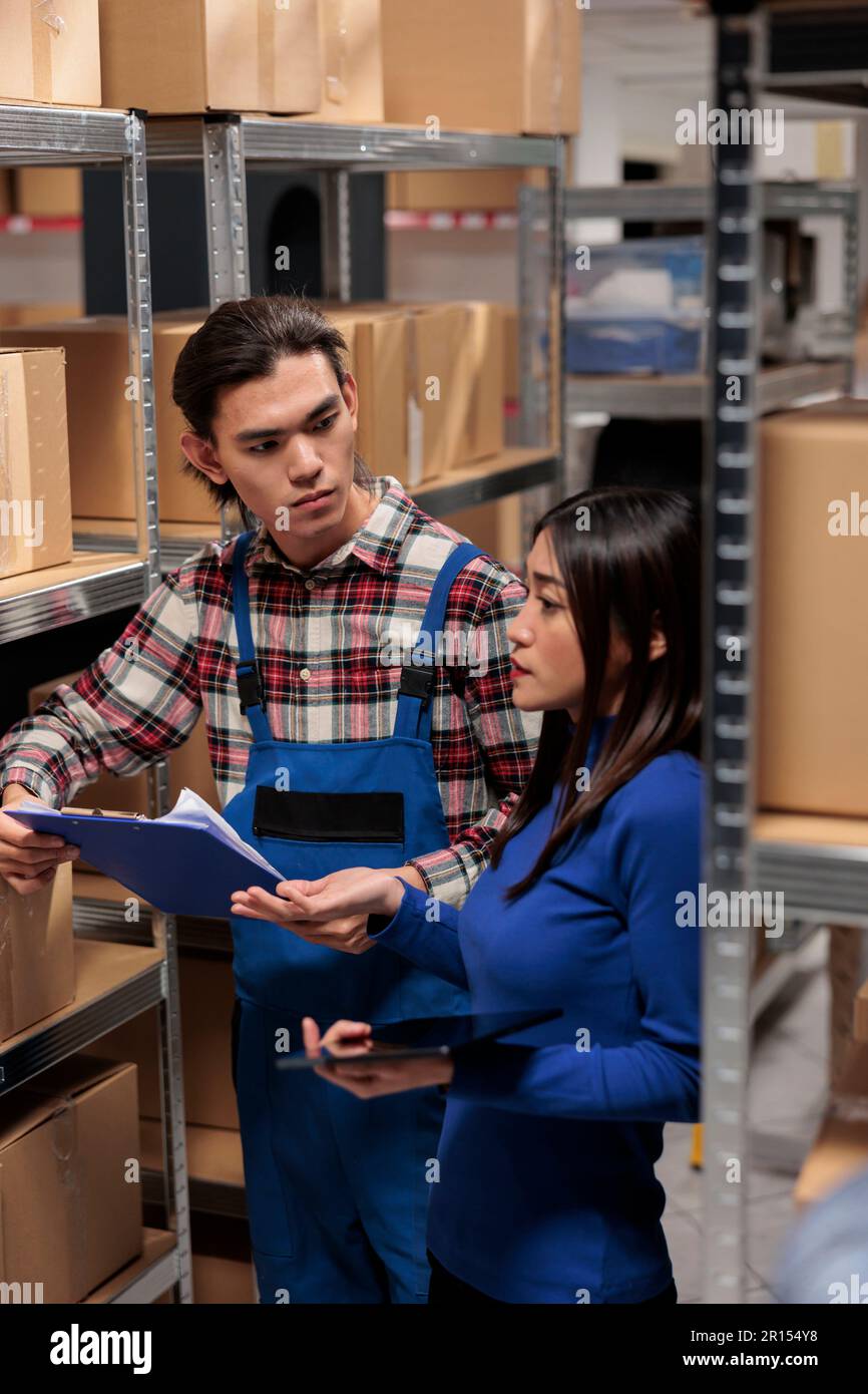 Homme et femme asiatiques qui font ensemble la gestion logistique d'entrepôt. Les employés du magasin collaborent tout en analysant le suivi des stocks et en comparant les données sur une tablette numérique et un presse-papiers Banque D'Images