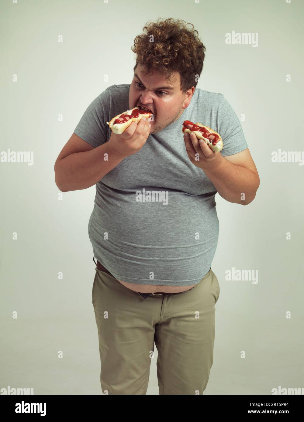La nourriture parfaite pour une journée de jeu. Studio photo d'un homme en surpoids mangeant deux hot dogs à la fois. Banque D'Images