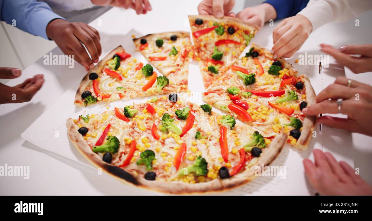Amis manger de la pizza à la table de bureau à l'intérieur Banque D'Images