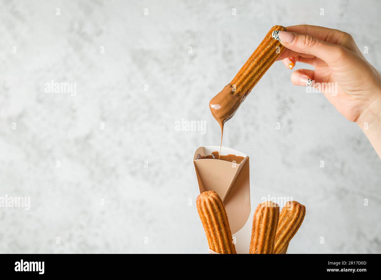 Femme prenant des churros d'un cône et le trempant dans une sauce au chocolat Banque D'Images