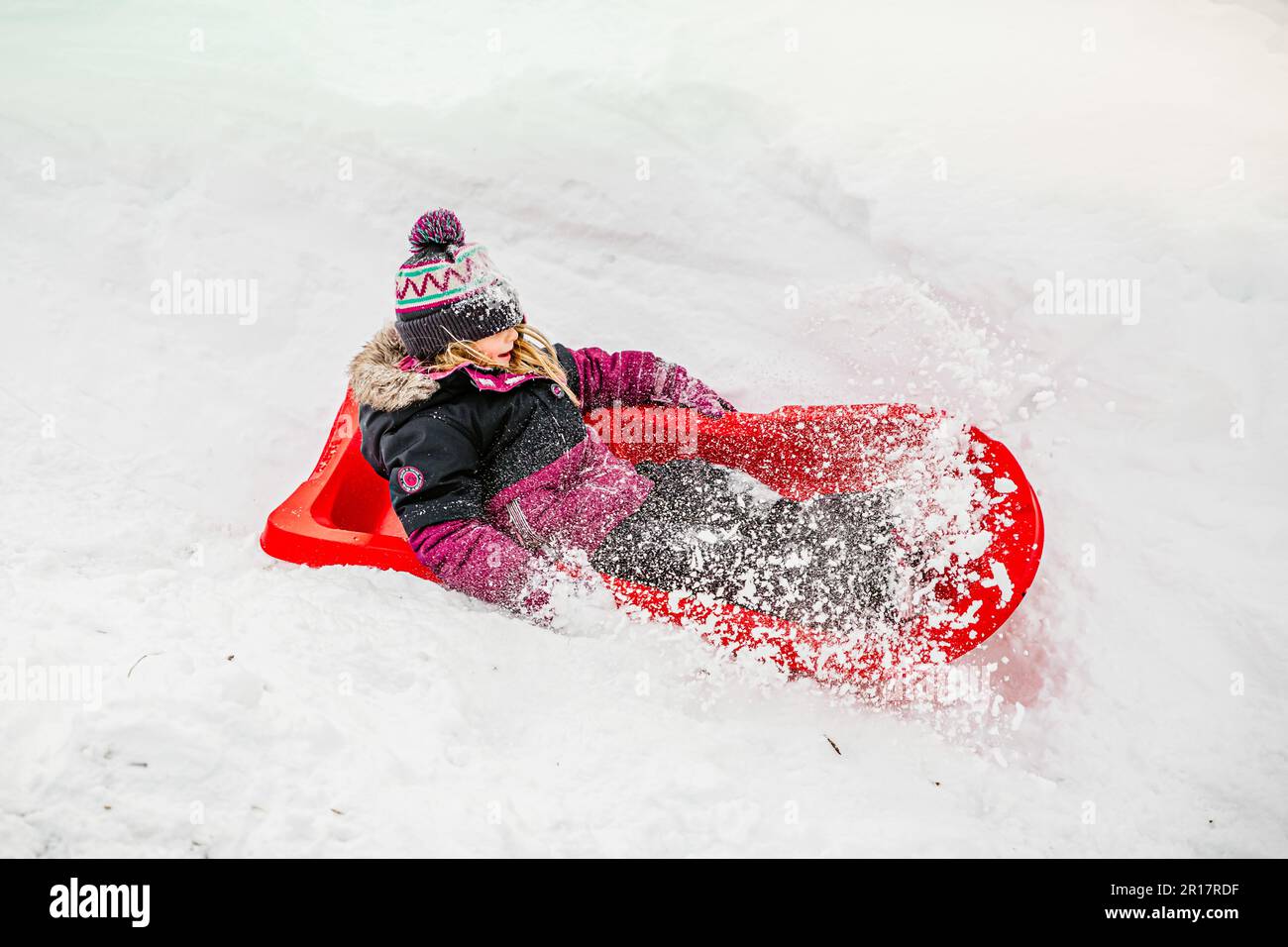 girld de 5 ans glissant sur un traîneau rouge lors d'une journée d'hiver Banque D'Images