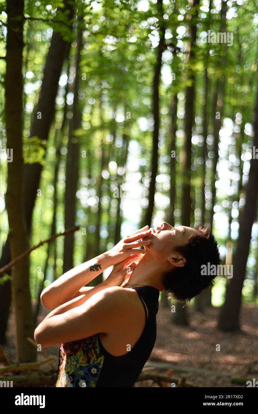 le danseur asiatique en maillot de corps se penche à nouveau à la lumière du vert forest Banque D'Images