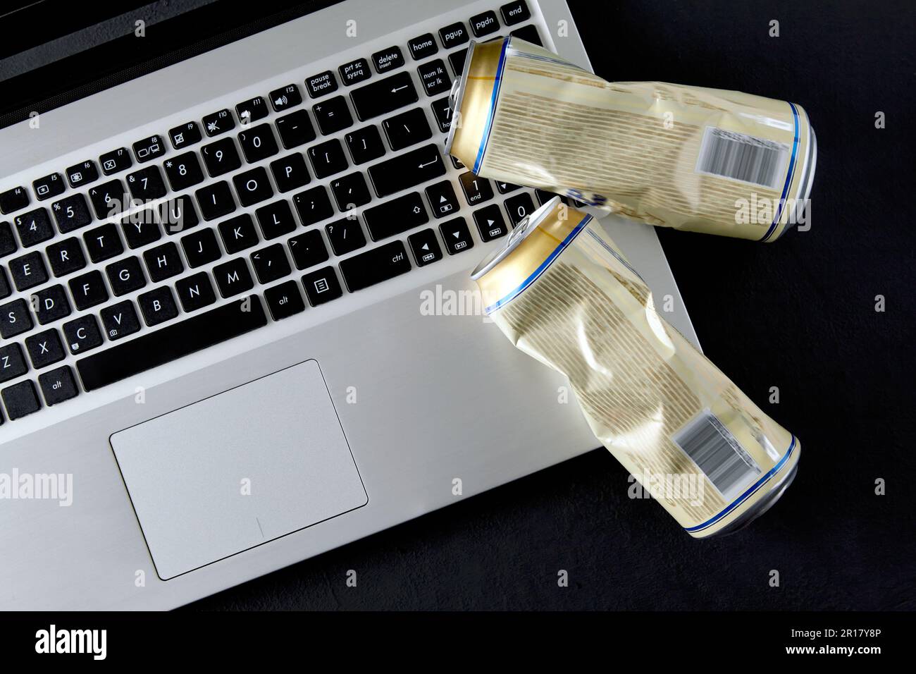 Vider les boîtes de bière écrasées sur un clavier d'ordinateur portable sur fond noir. Des combats en contrebas sur les médias sociaux. Vue de dessus avec espace de copie Banque D'Images