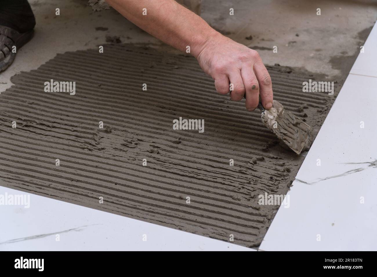Un ouvrier de la construction applique du ciment pour la pose de carreaux de céramique de plancher avec une spatule. Mise au point sélective Banque D'Images