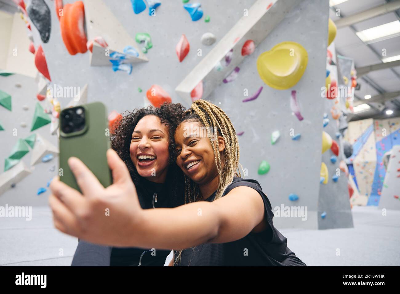 Deux amies souriantes posant pour Selfie par le mur d'escalade au centre d'activités intérieur Banque D'Images