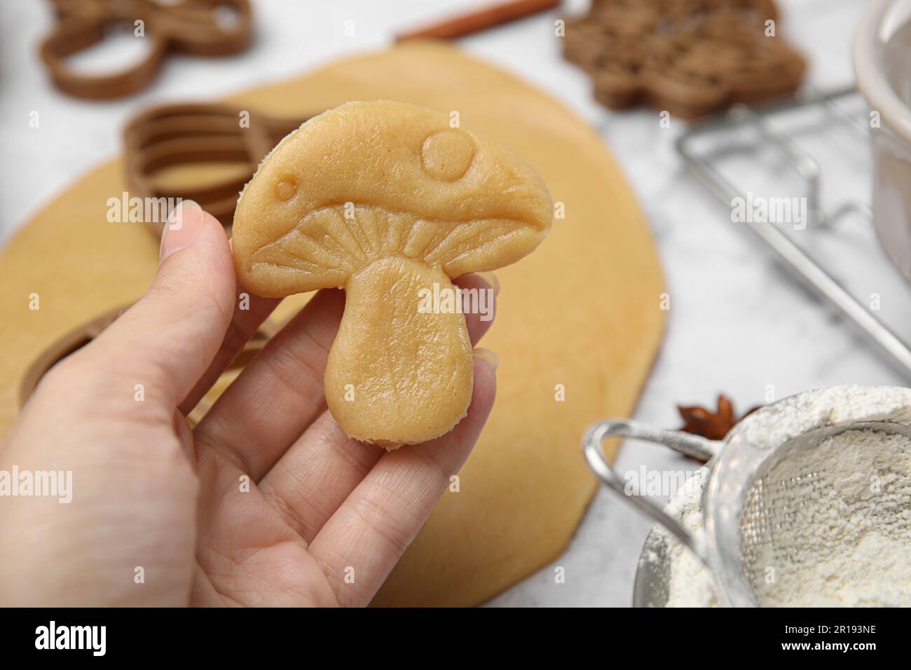 Femme tenant un biscuit en forme de champignon non cuit à la table blanche, gros plan Banque D'Images