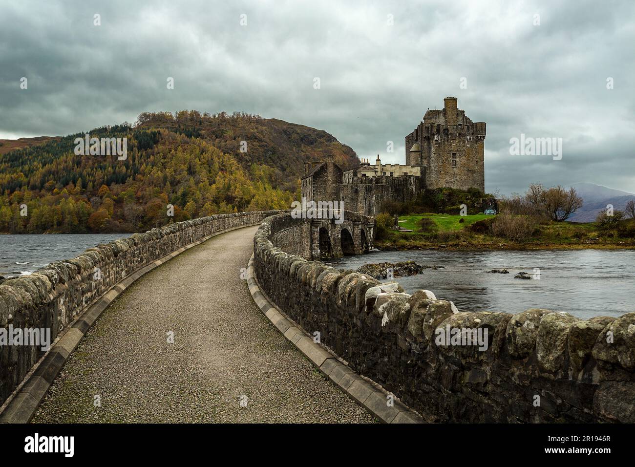 Ancien château écossais d'Eilean Donan situé près de Dornie, un pont en pierre mène au château et une rivière passe sous celui-ci. Une colline avec des arbres sur son slop Banque D'Images