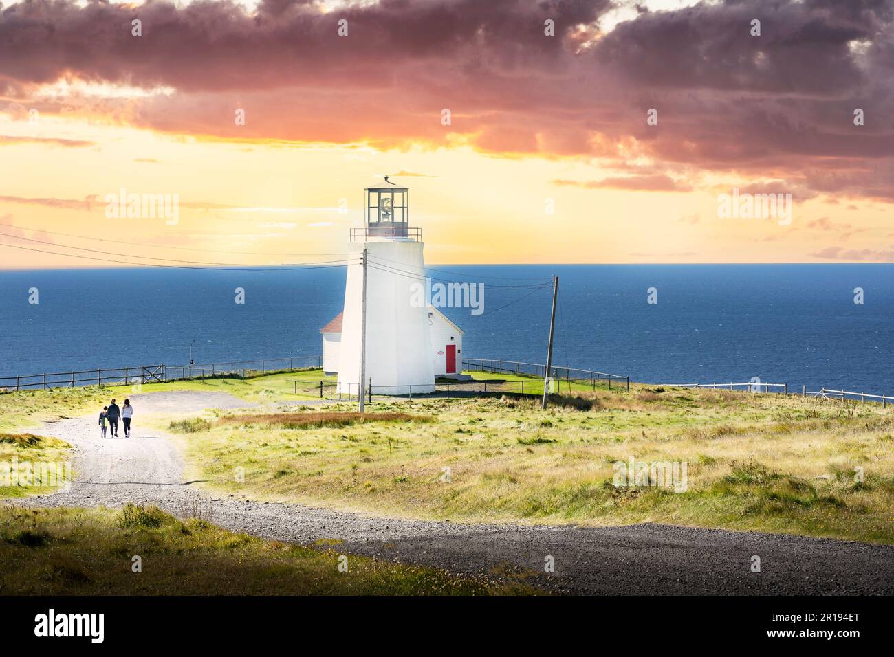 Coucher du soleil groupe de touristes marchant le long d'une route de gravier vers un phare le long de la côte est canadienne à Cape St. Mary's Terre-Neuve Canada. Banque D'Images