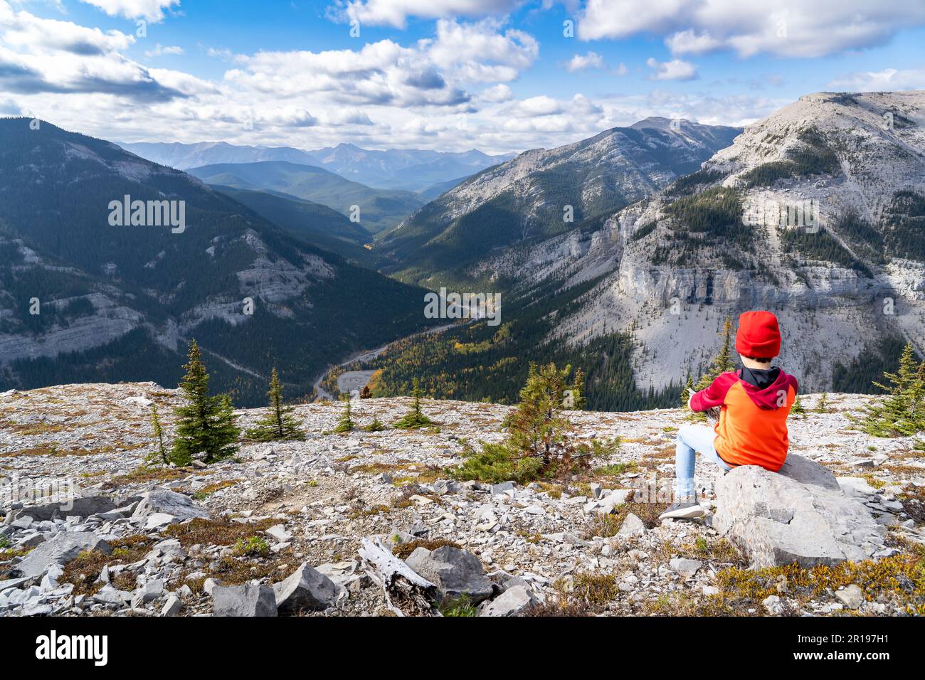 Jeune garçon assis sur un rocher surplombant une montagne vally dans les Rocheuses canadiennes à Moose Mountain Kananaskis Alberta. Banque D'Images