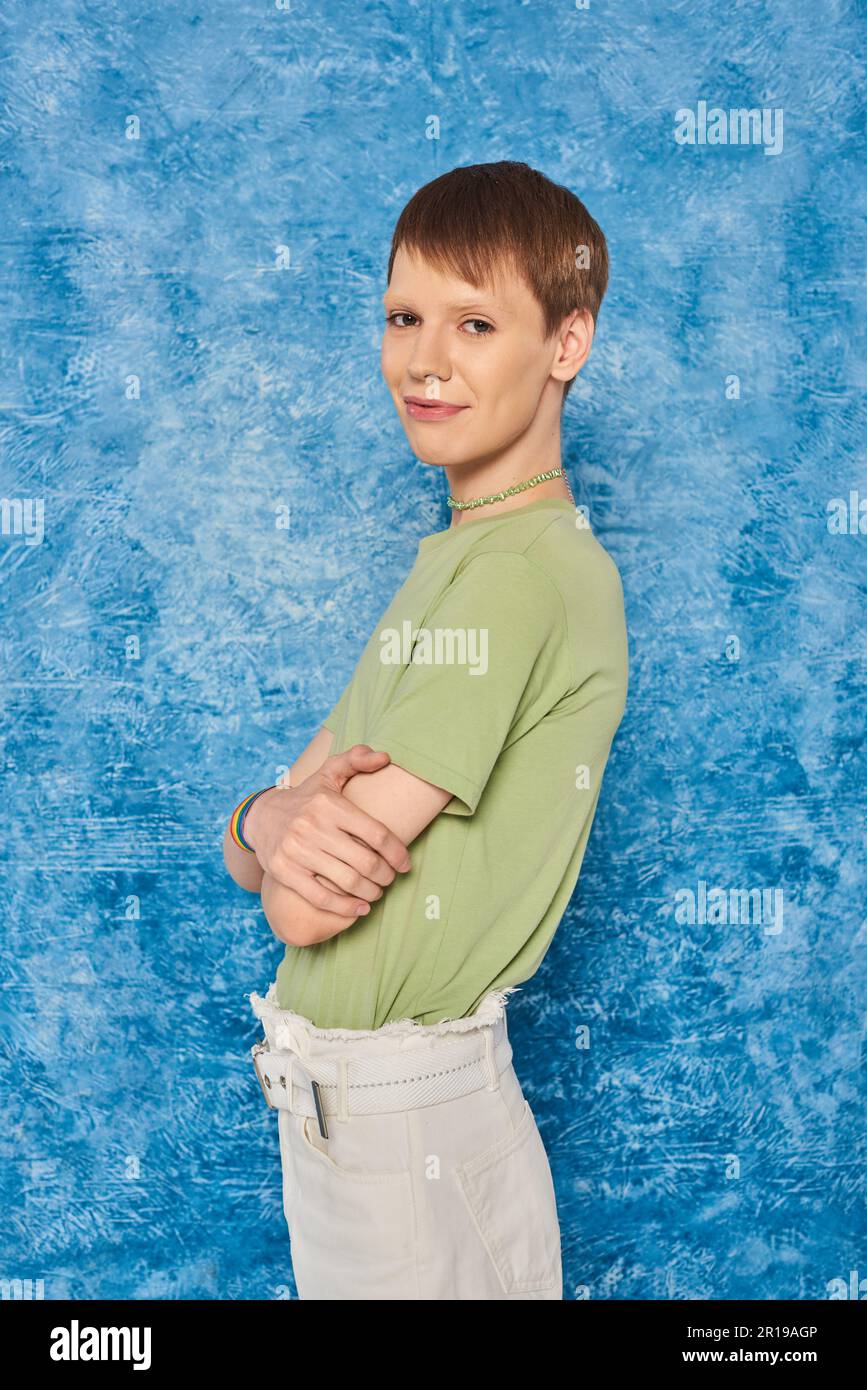 Personne souriante dans des vêtements décontractés croisant les bras et souriant à l'appareil photo tout en célébrant le mois de la fierté et debout sur fond bleu marbré Banque D'Images