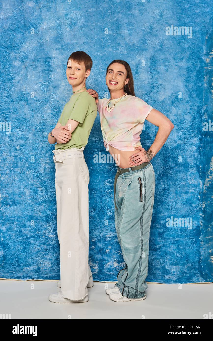 Homme homosexuel plein de style et de gaieté qui épouse les bras croisés tout en célébrant l'orgueil ensemble sur fond bleu texturé Banque D'Images