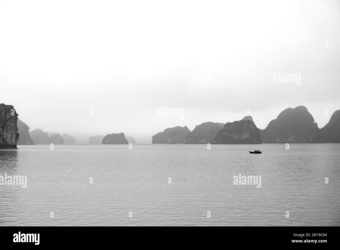 Petit bateau de pêche local isolé en mer avec toile de fond des îles calcaires typiques de Bai Tu long Bay, baie d'Halong, Vietnam. Banque D'Images