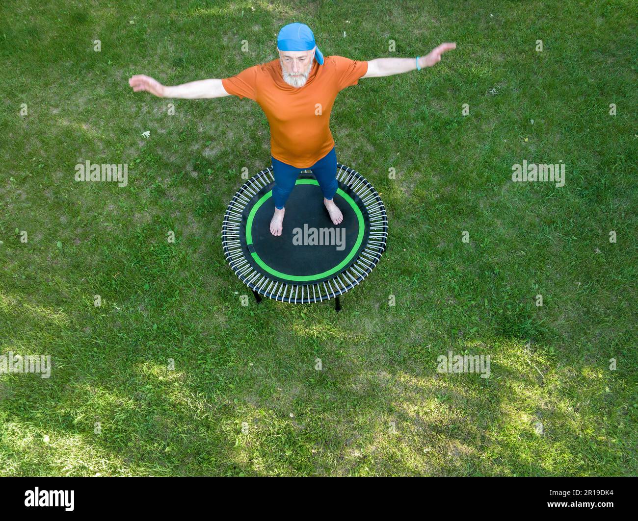 senior surpoids homme s'exerçant sur un mini trampoline dans son arrière-cour, fitness et rebondissement concept, vue aérienne Banque D'Images