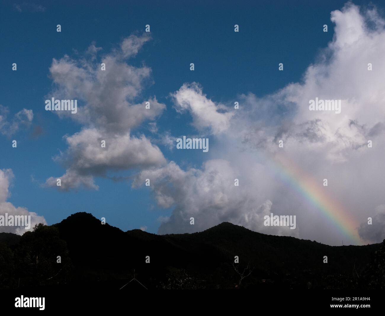 Silhouette d'une montagne andine avec un segment d'un arc-en-ciel et des nuages Banque D'Images