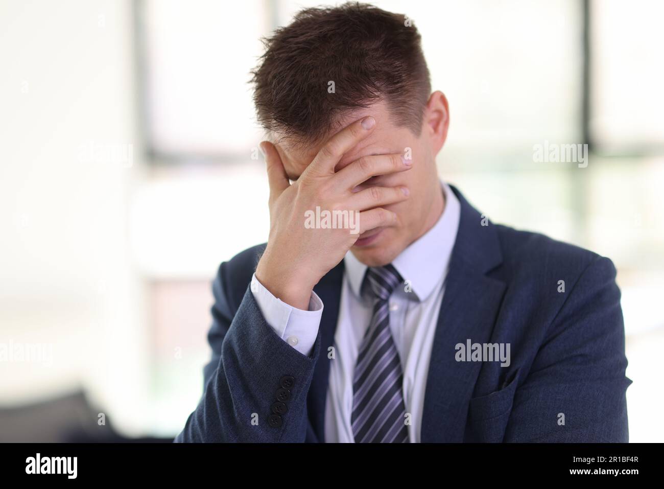 L'homme dépressif en costume habillé couvre le visage avec la paume dans le bureau Banque D'Images
