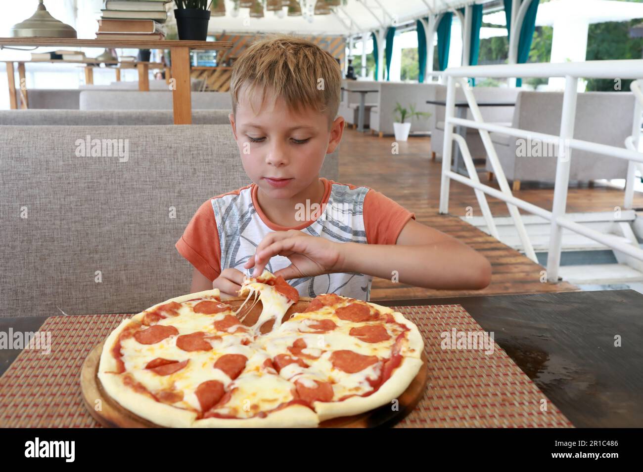 Un enfant mange une pizza au pepperoni dans un restaurant Banque D'Images