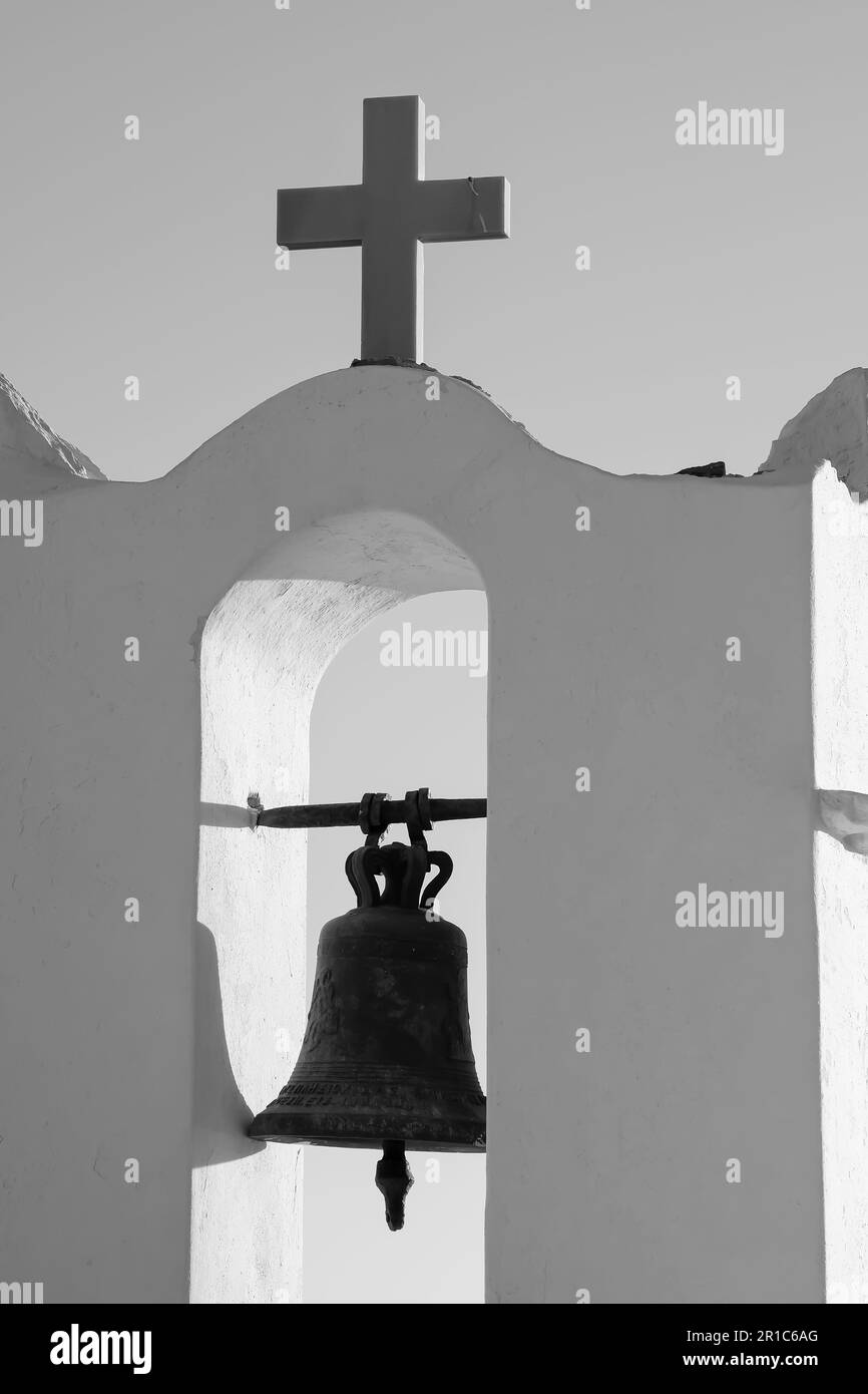 Vue sur une croix religieuse et une cloche au sommet d'une ancienne église orthodoxe grecque blanchie à la chaux dans iOS Grèce en noir et blanc Banque D'Images