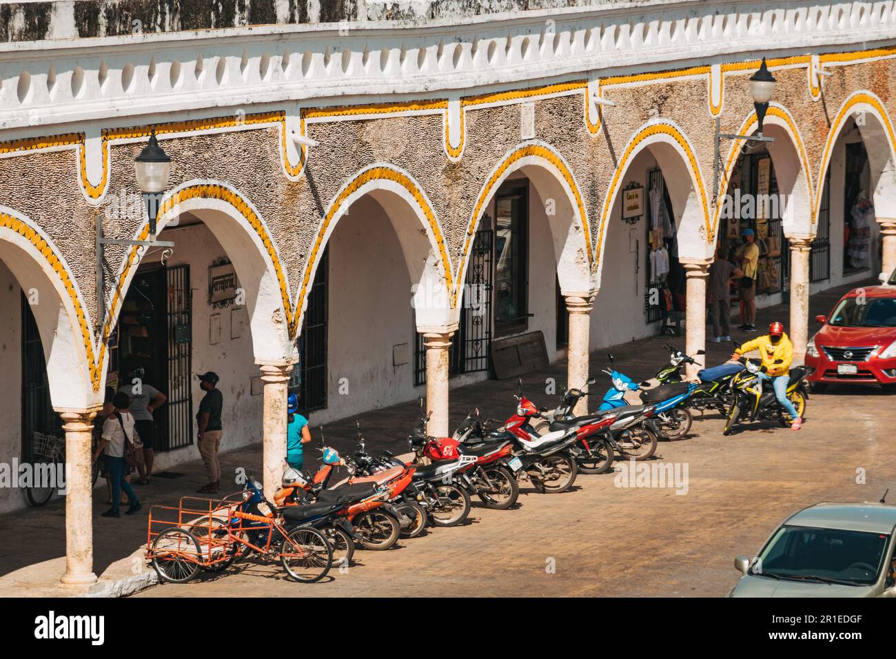 Passerelle à arcades à Izamal, Mexique, avec des arches blanches, des garnitures jaunes et des murs texturés de pierre, surplombant une rangée de motos garées Banque D'Images