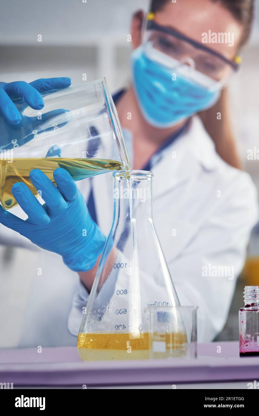 J'espère que rien ne va mal. une femme scientifique méconnaissable portant un masque de protection tout en mélangeant des produits chimiques à l'intérieur d'un laboratoire. Banque D'Images