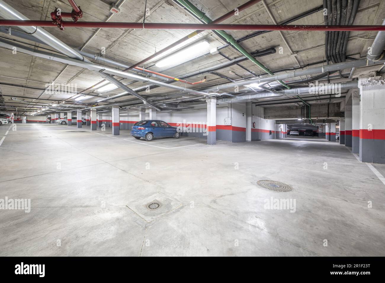 Quelques places de parking d'un grand garage dans un immeuble résidentiel urbain avec des colonnes et des frontières blanches et rouges Banque D'Images