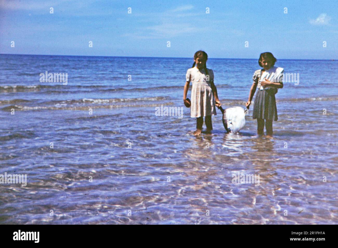 Deux jeunes filles debout dans l'eau, tenant un poisson de lune (ou Opah poisson) qui a été utilisé pour faire du savon ca. 1950-1955 Banque D'Images