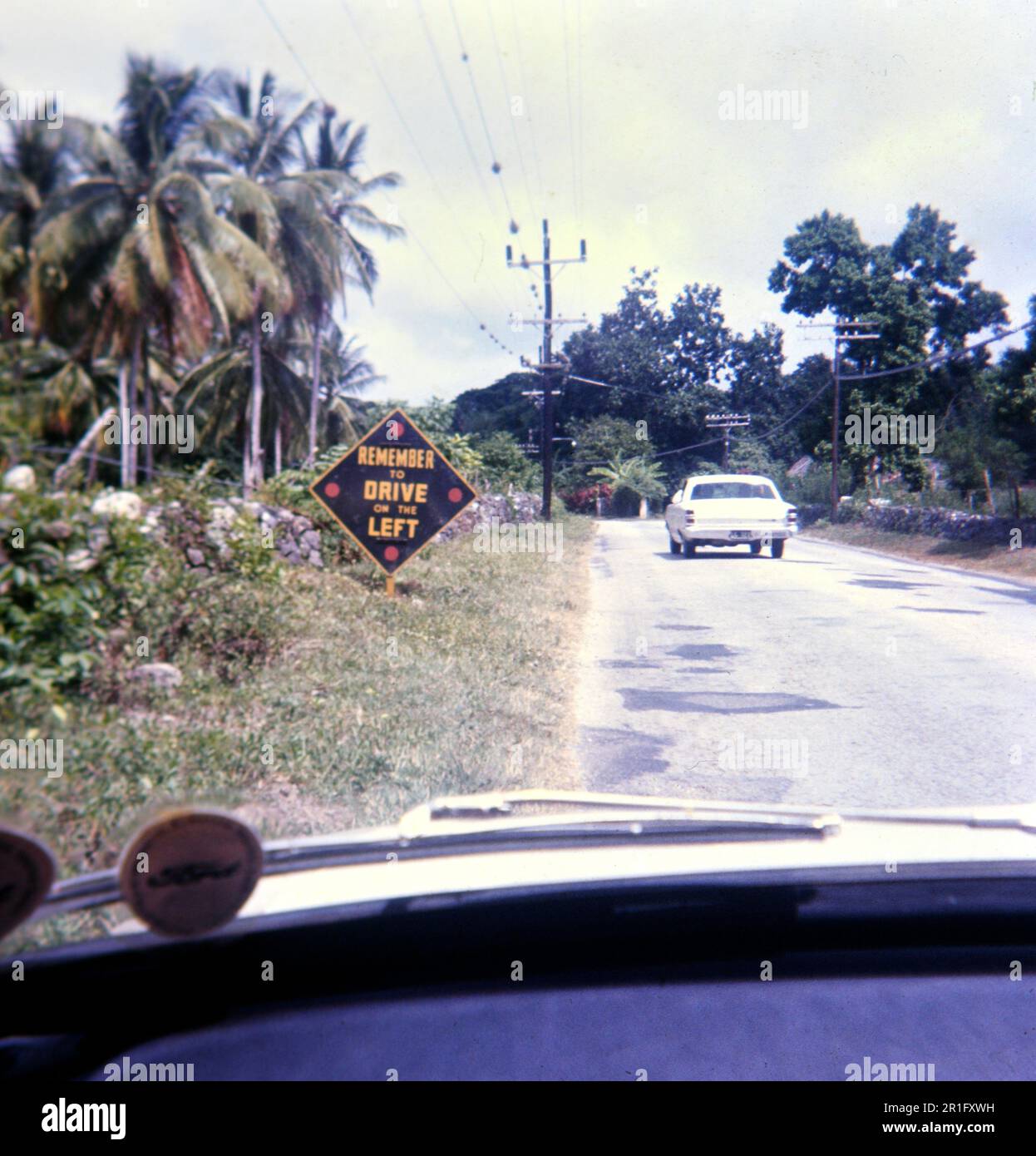 Un touriste américain prend une photo, tout en conduisant, d'un panneau rappelant aux visiteurs de conduire sur le côté gauche de la route pendant qu'ils se trouvent à la Jamaïque ca. 1969 Banque D'Images