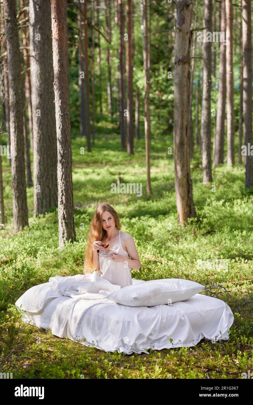 Une femme se réveille dans une forêt d'été. Une fille boit le thé du matin assis sur un matelas dans les bois Banque D'Images