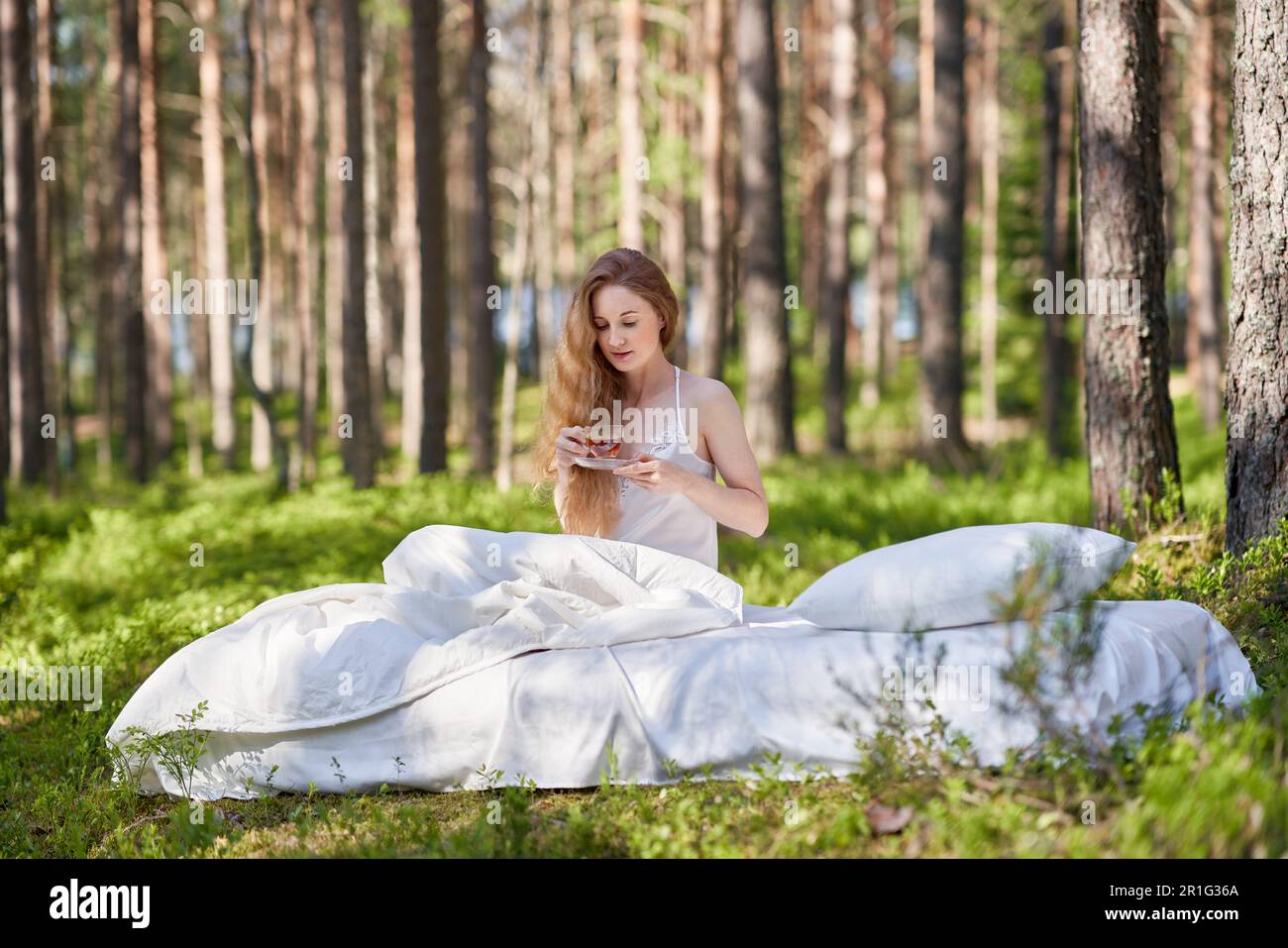 Une femme se réveille dans une forêt d'été. Une fille boit le thé du matin assis sur un matelas dans les bois Banque D'Images