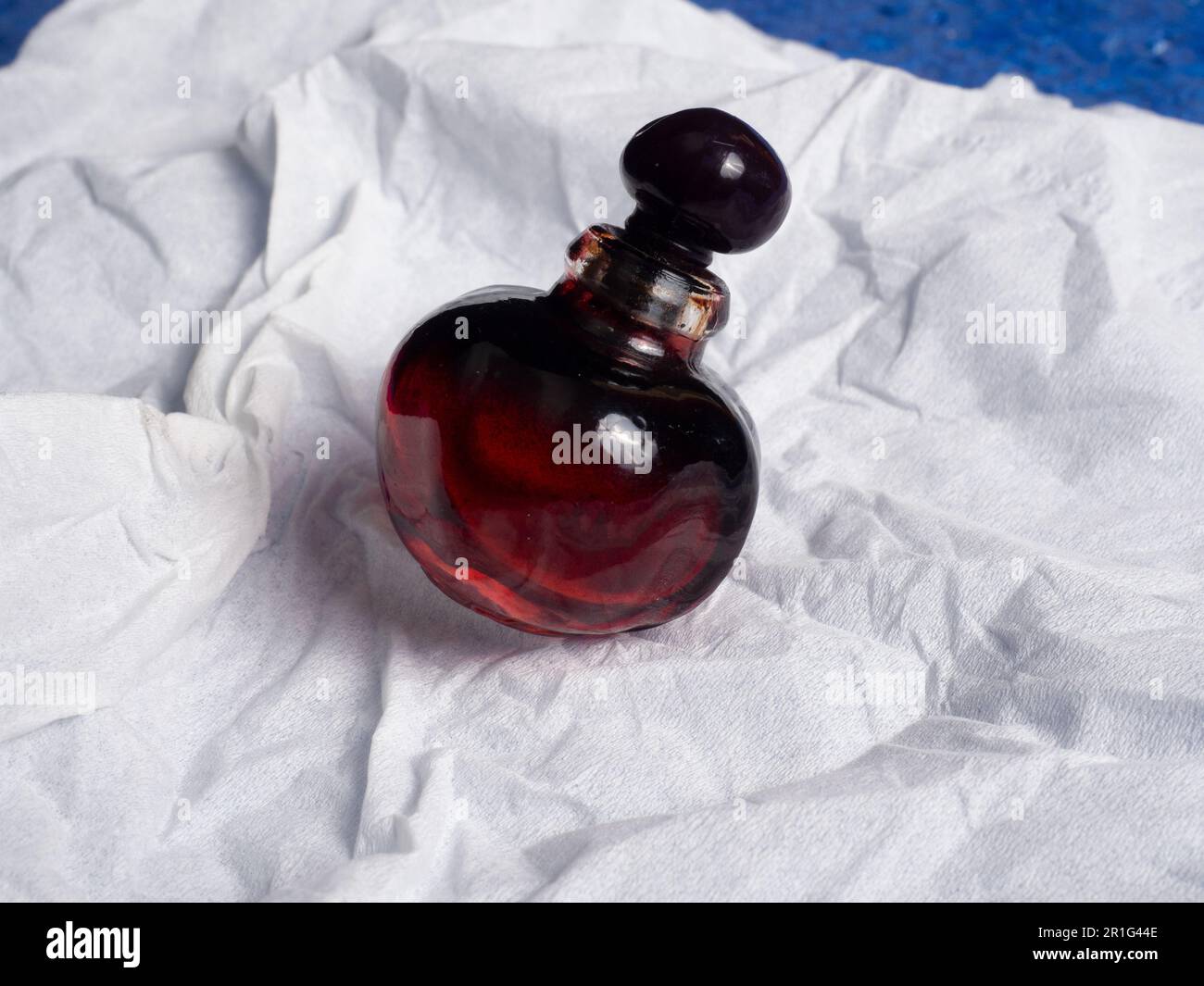 Photo d'une belle bouteille de parfum en forme de cerise sur un tissu blanc Banque D'Images