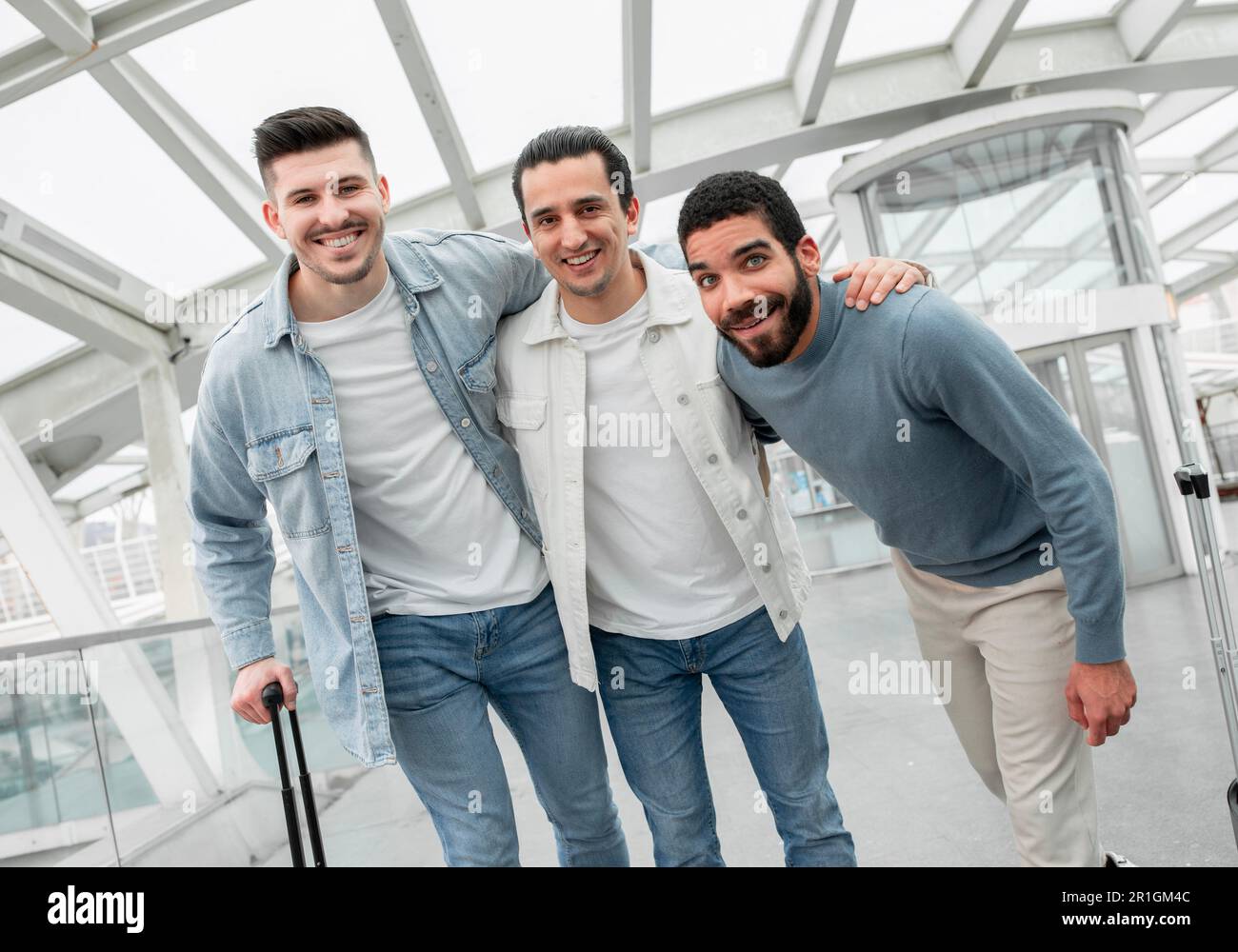 Touristes hommes Trio embrassant posant avec des bagages dans l'aéroport moderne Banque D'Images