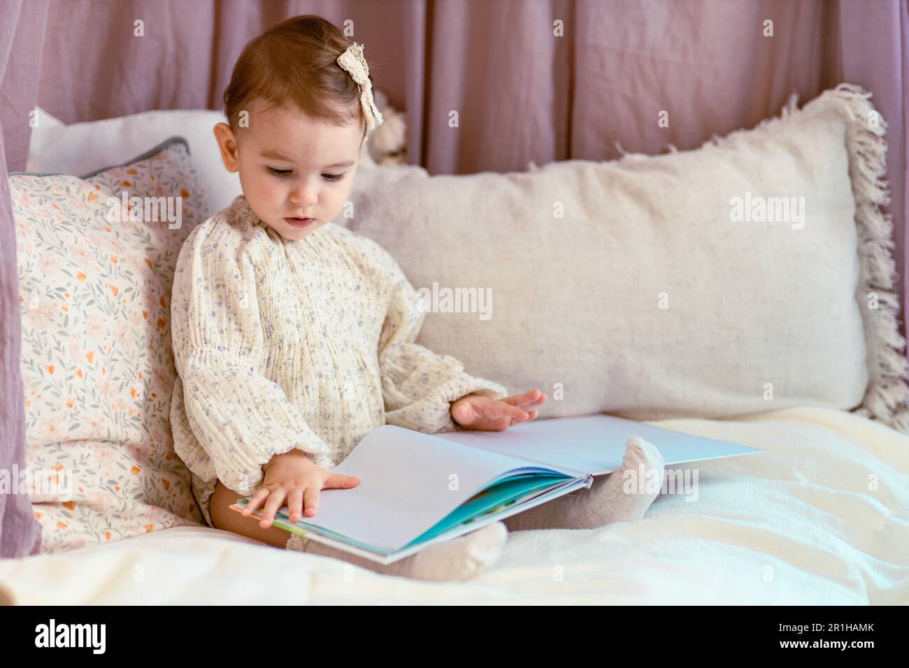 Mignon, petite fille de bébé assis sur les oreillers lisant un livre Banque D'Images