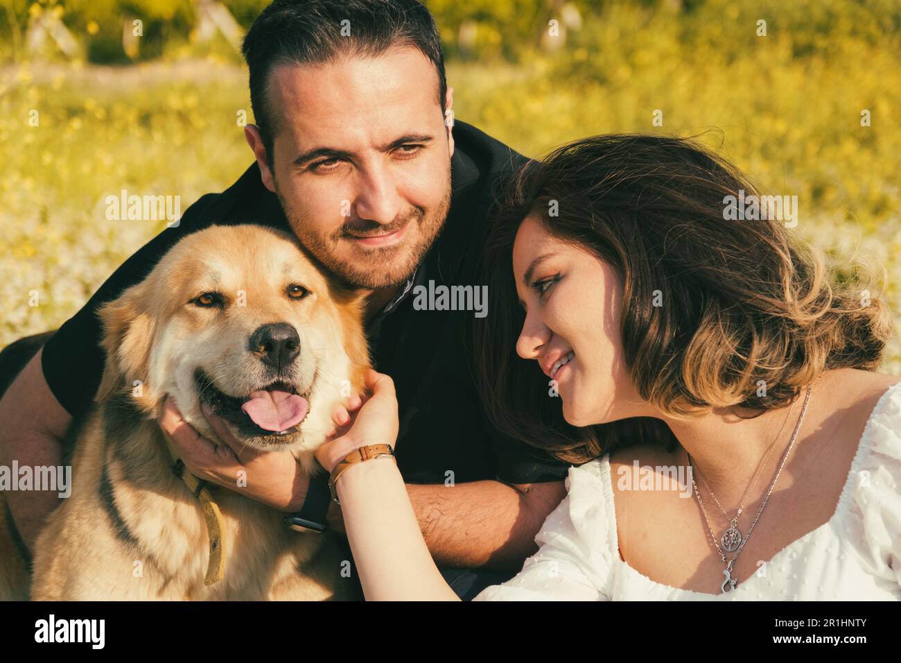 Sur une couverture de pique-nique blanche, une femme enceinte et son mari partagent un moment de tendresse, tandis que leur chien amical cherche l'affection à proximité Banque D'Images