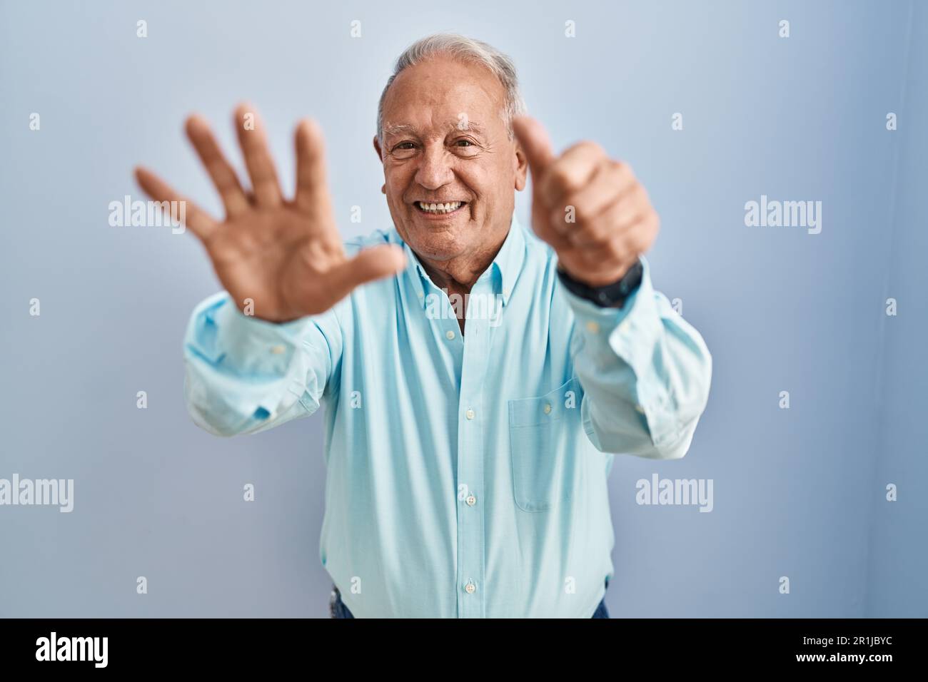 Homme âgé avec des cheveux gris debout sur fond bleu montrant et pointant vers le haut avec les doigts numéro six tout en souriant confiant et heureux. Banque D'Images