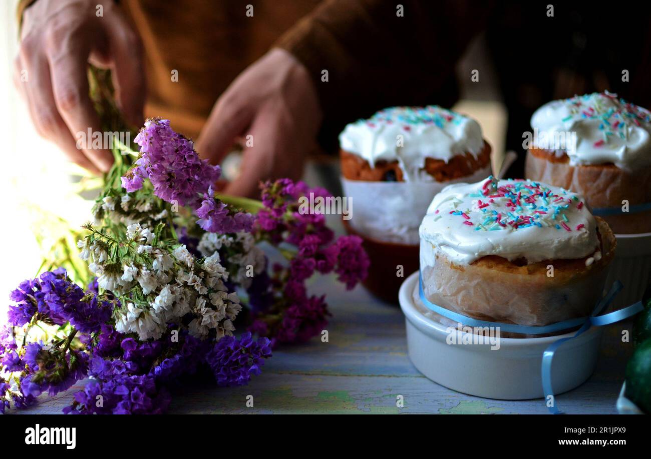 Trois gâteaux de Pâques pour les vacances sont sur la table. Les mains d'un homme tiennent un bouquet d'immortelle. Fleurs de différentes couleurs Banque D'Images
