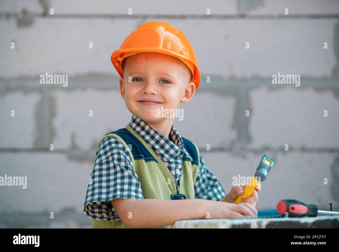 Mignon petit enfant dans un casque de constructeur avec outils de  réparation sur le chantier de construction. Enfant garçon dans un casque de  construction qui travaille dur. Des enfants souriants Photo Stock 