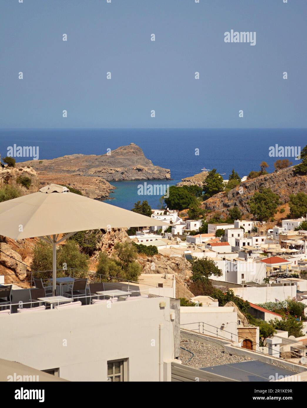 Panorama du village grec de Lindos avec des maisons blanches et des arbres verts au pied de la colline.les rochers et les bateaux touristiques sont visibles dans la baie. Banque D'Images