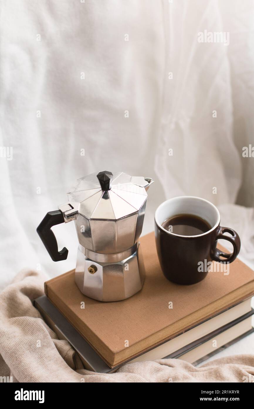 Une tasse de café et un pot de moka sur quelques livres dans un espace confortable. Profiter de la vie à l'intérieur. Banque D'Images