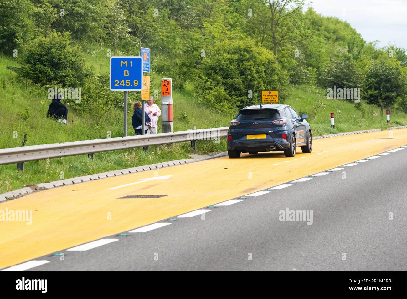 Smart autoroutier Royaume-Uni - voiture en panne garée dans une zone de refuge orange et passagers debout derrière une barrière anti-collision sur la section d'autoroute intelligente de M1 Banque D'Images