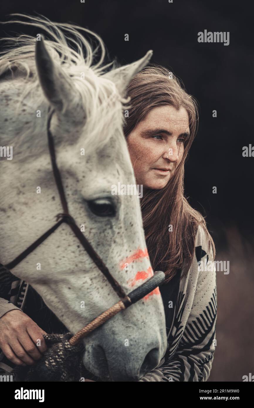 Portrait d'une femme sur sa peinture de guerre indienne d'origine américaine décorée de cheval arabe blanc au printemps en plein air Banque D'Images