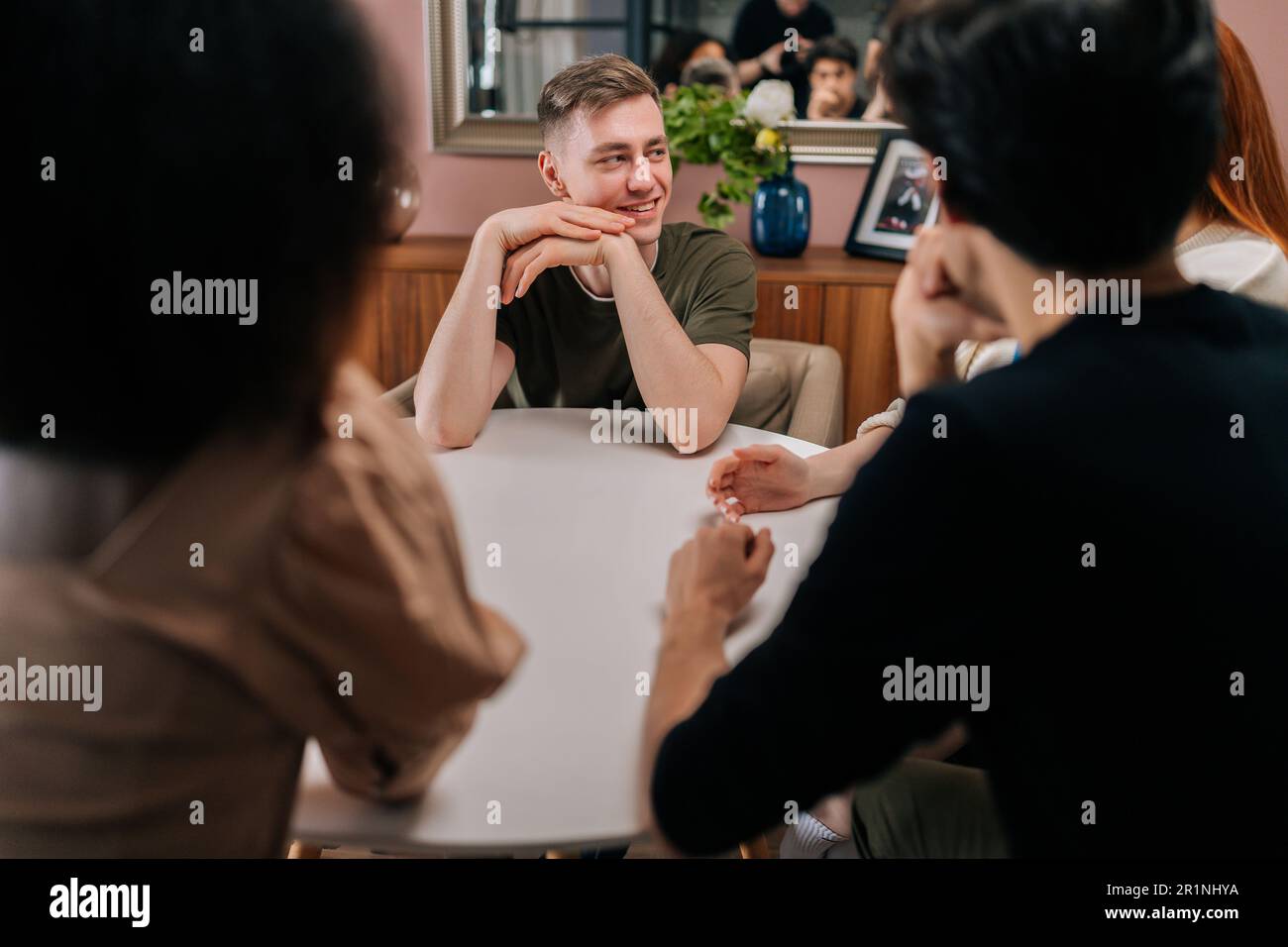 Vue de face d'un beau jeune homme assis autour d'une table avec des amis multiethniques, racontant des histoires, traînez avec des hommes et des femmes en profitant de temps libre. Banque D'Images