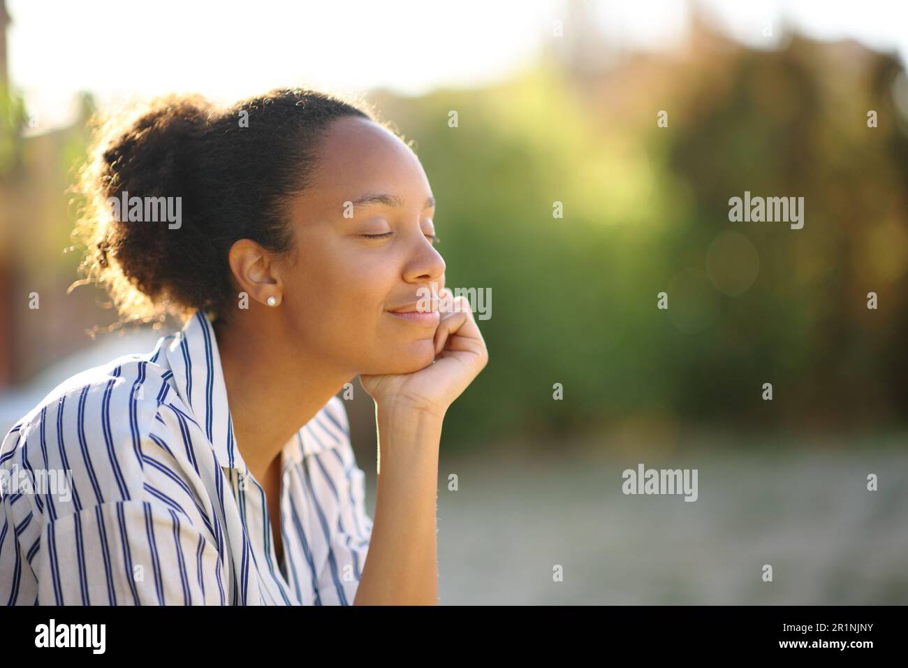Femme noire détendue se reposant seule dans un parc au coucher du soleil Banque D'Images