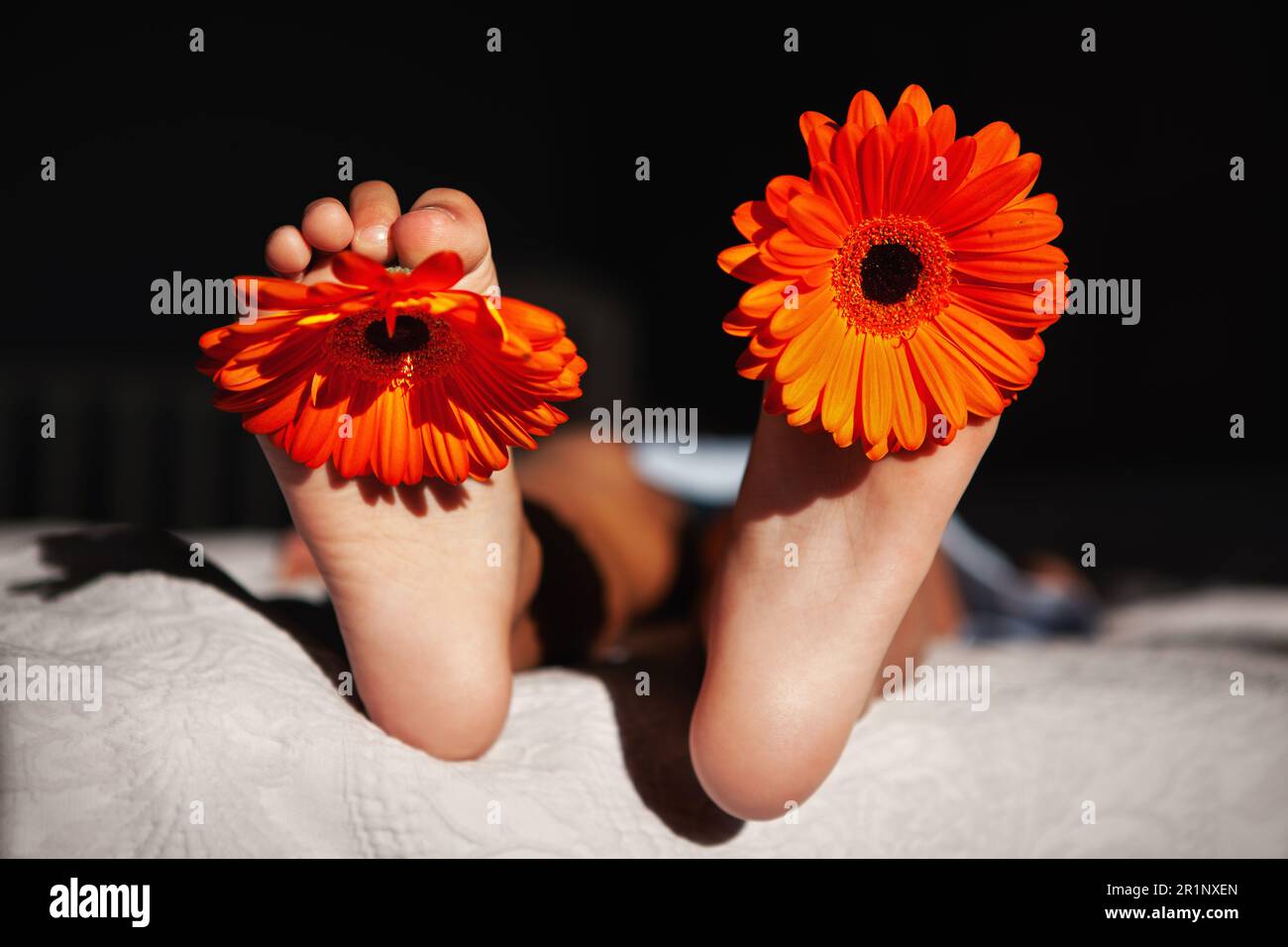 Gros plan sur le pied de l'enfant avec des pâquerettes orange et vibrantes aux rayons chauds du soleil. Banque D'Images