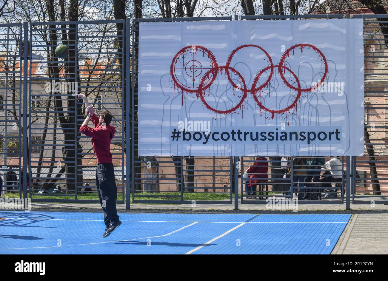 Une personne joue au basket-ball sur fond de bannière avec l'inscription #BoycottRussianSport dans l'un des terrains de sport de Lviv. L’Ukraine et de nombreux pays dans le monde exigent que les athlètes russes soient interdits aux Jeux Olympiques et autres compétitions internationales en raison de la guerre russo-ukrainienne lancée par la Russie. De nombreux athlètes ukrainiens qui ont défendu l'Ukraine contre l'agresseur russe sont déjà morts dans cette guerre. Pour soutenir le boycott, une bannière portant l'inscription #BoycottRussianSport a été accrochée à l'un des terrains de sport de Lviv. Banque D'Images
