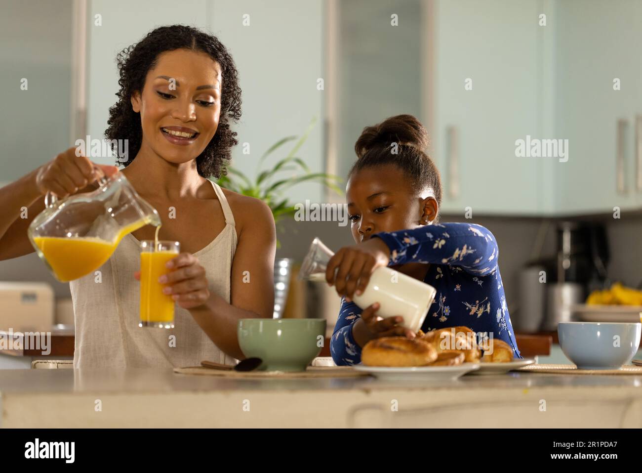 Bonne mère afro-américaine et fille assises sur l'île de la cuisine pour prendre le petit déjeuner ensemble Banque D'Images
