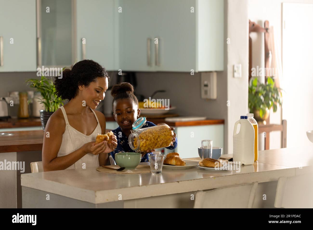Bonne mère afro-américaine et fille assises sur l'île de la cuisine pour prendre le petit déjeuner ensemble Banque D'Images