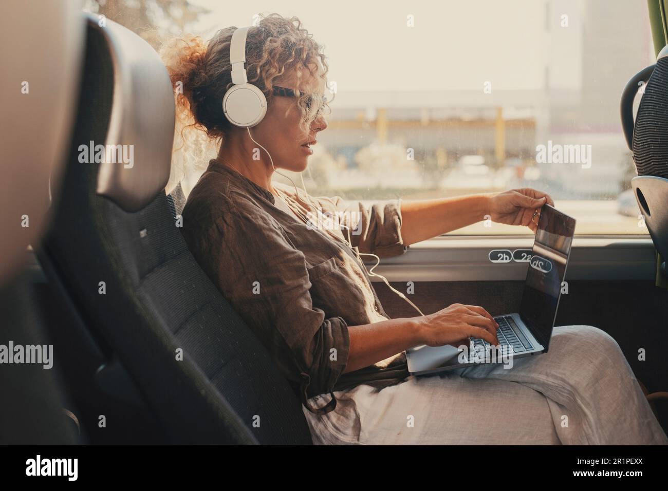 Femme d'âge moyen, ordinateur à l'intérieur du véhicule de transport en bus pendant les voyages d'affaires ou de vacances. Style de vie numérique professionnel moderne. Les femmes avec casque apprécient le transport. Femme voyageur avec ordinateur portable Banque D'Images