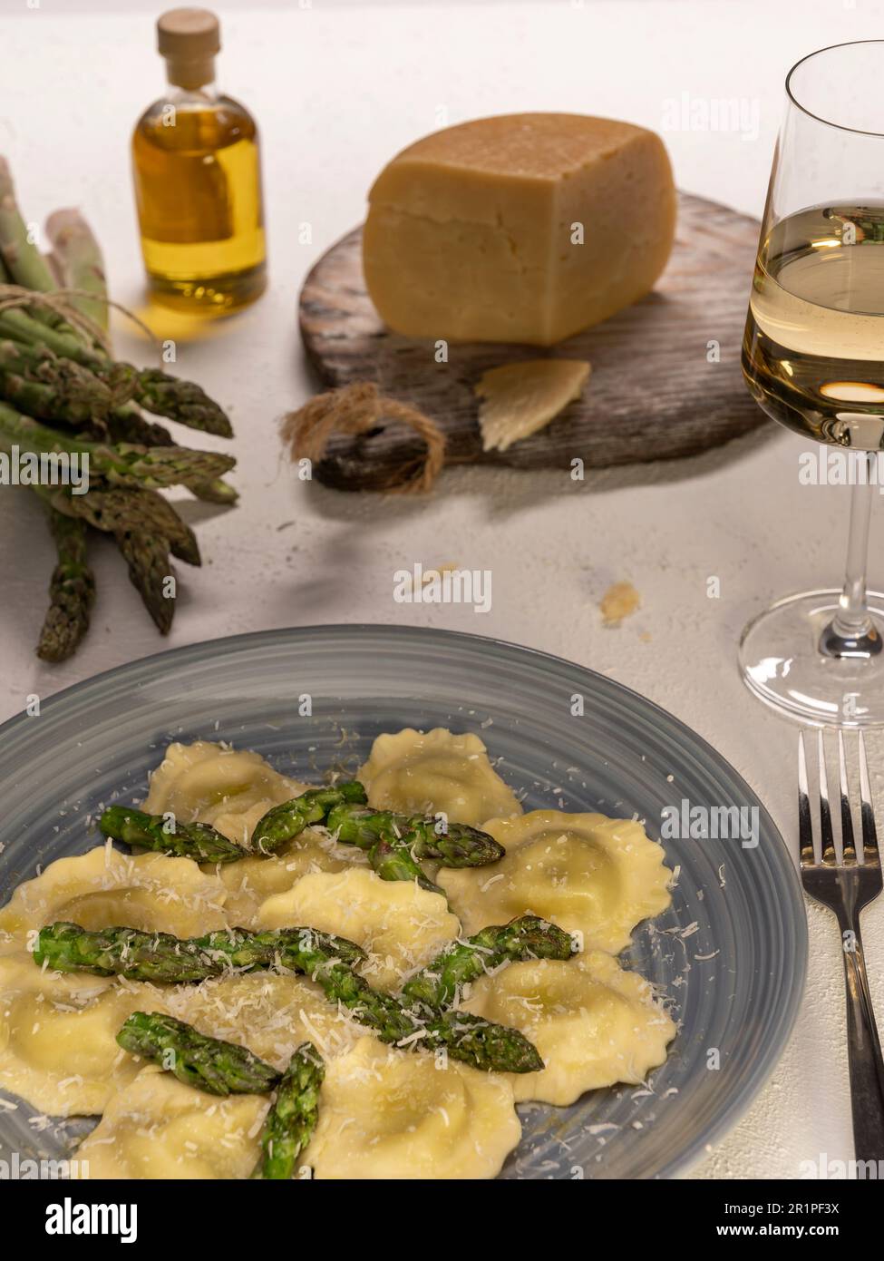 Tortellini aux asperges frites, servi avec du vin blanc et décoré d'asperges fraîches, d'huile d'olive et de parmesan Banque D'Images
