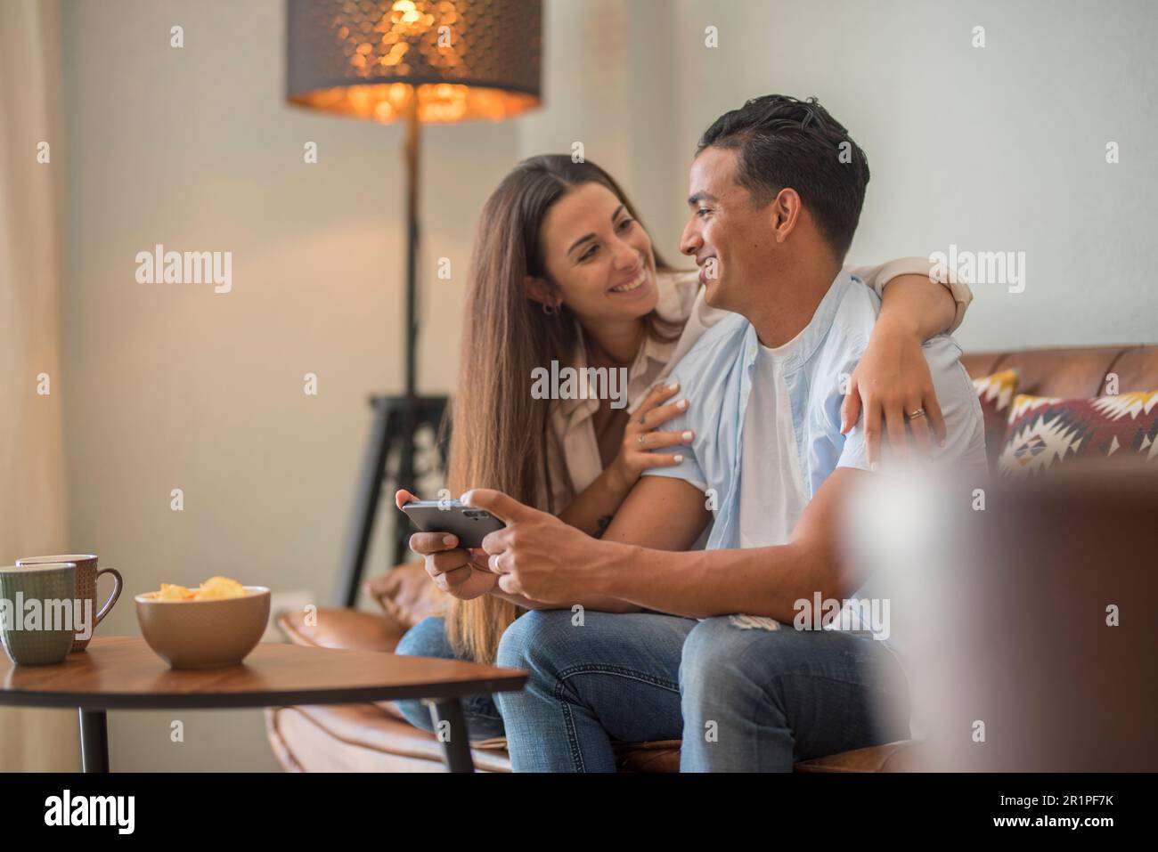 Couple amoureux reposant sur un canapé confortable, amusant, applications pour smartphone, profiter de la vidéo à distance, garçon montrant site Web intéressant à la petite amie, choisir des biens de services en ligne e-commerce concept Banque D'Images